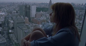 Movie still from “Lost in Translation” (2003), directed by Sofia Coppola – A woman sitting on top of a building looking out over a city; Medium shot, High angle