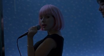 Movie still from “Lost in Translation” (2003), directed by Sofia Coppola – A woman with pink hair is singing into a microphone; Medium shot, Over the shoulder angle
