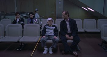 Movie still from “Lost in Translation” (2003), directed by Sofia Coppola – Two men sitting in a waiting room with a woman; Wide shot, High angle