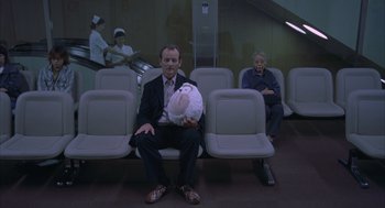 Movie still from “Lost in Translation” (2003), directed by Sofia Coppola – A man sitting on a bench holding a stuffed animal; Medium shot, Overhead angle