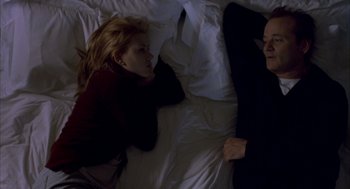 Movie still from “Lost in Translation” (2003), directed by Sofia Coppola – Two people laying in a bed on a white comforter; Medium shot, Overhead angle