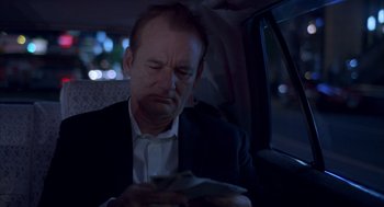 Movie still from “Lost in Translation” (2003), directed by Sofia Coppola – A man sitting in the back seat of a car looking at his cell phone; Close Up shot, Over the shoulder angle