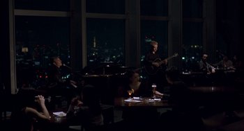 Movie still from “Lost in Translation” (2003), directed by Sofia Coppola – A group of people sitting at tables in front of a window; Extreme Wide shot, High angle