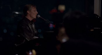Movie still from “Lost in Translation” (2003), directed by Sofia Coppola – A man sitting in front of a microphone on a stage; Medium shot, High angle