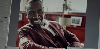 Movie still from “Lupin” (2021), created by Tigran Rosine – A man sitting in a chair smiling for the camera; Close Up shot, Low angle