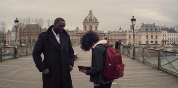Movie still from “Lupin” (2021), created by Tigran Rosine – A man and a woman standing next to each other on a bridge; Medium shot, Over the shoulder angle