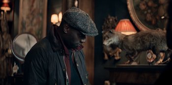 Movie still from “Lupin” (2021), created by Tigran Rosine – A man wearing a hat and jacket in a room; Close Up shot, Low angle