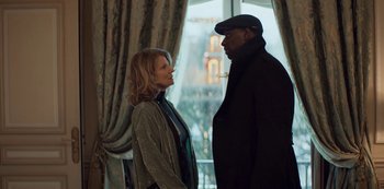 Movie still from “Lupin” (2021), created by Tigran Rosine – A man and a woman standing next to each other in front of a window; Medium shot, Over the shoulder angle
