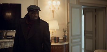 Movie still from “Lupin” (2021), created by Tigran Rosine – A man wearing a black coat and a hat; Medium shot, Low angle