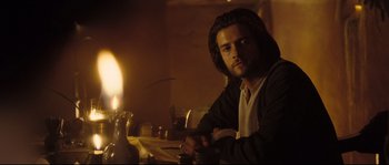 Movie still from “Kingdom of Heaven” (2005), directed by Ridley Scott – A man sitting at a table with a candle in the background; Medium shot, Over the shoulder angle