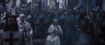 Movie still from “Kingdom of Heaven” (2005), directed by Ridley Scott – A group of men in medieval garb standing around a woman; Wide shot, High angle