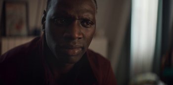 Movie still from “Lupin” (2021), created by Tigran Rosine – A person wearing a red shirt; Close Up shot, Over the shoulder angle