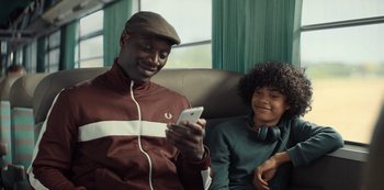 Movie still from “Lupin” (2021), created by Tigran Rosine – A man and a woman sitting in a chair looking at a phone; Medium shot, Over the shoulder angle