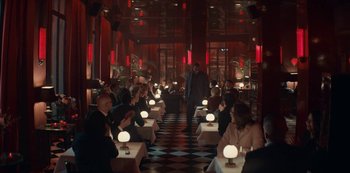 Movie still from “Lupin” (2021), created by Tigran Rosine – People are sitting at tables in a dimly - lit restaurant; Extreme Wide shot, Over the shoulder angle