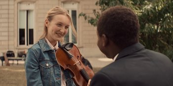 Movie still from “Lupin” (2021), created by Tigran Rosine – A woman holding up a violin to a young man; Close Up shot, Over the shoulder angle