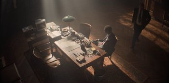 Movie still from “Lupin” (2021), created by Tigran Rosine – A man sitting at a table with papers on it; Wide shot, High angle