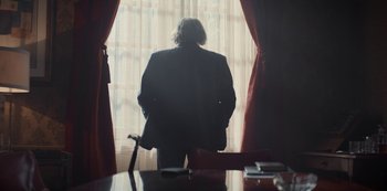 Movie still from “Lupin” (2021), created by Tigran Rosine – A man standing in front of a window with red drapes; Medium shot, Over the shoulder angle