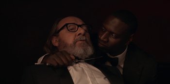 Movie still from “Lupin” (2021), created by Tigran Rosine – A man with a beard and a man in a suit and bow tie; Close Up shot, Over the shoulder angle