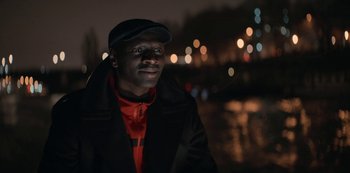 Movie still from “Lupin” (2021), created by Tigran Rosine – A man wearing a hat and a red shirt; Close Up shot, Low angle