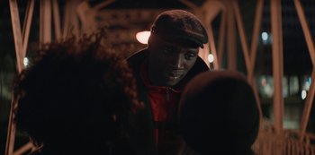 Movie still from “Lupin” (2021), created by Tigran Rosine – A man wearing a cap and jacket is looking at the camera; Close Up shot, Over the shoulder angle