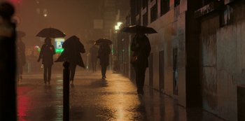 Movie still from “Lupin” (2021), created by Tigran Rosine – A group of people walking down a street holding umbrellas; Extreme Wide shot, Low angle