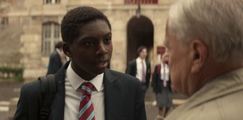 Movie still from “Lupin” (2021), created by Tigran Rosine – A man in a suit and tie talking to another man in a suit and tie; Close Up shot, Over the shoulder angle