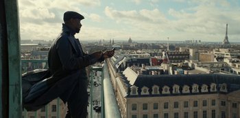 Movie still from “Lupin” (2021), created by Tigran Rosine – A man standing on a balcony looking at his cell phone; Medium shot, Low angle