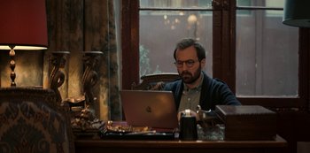 Movie still from “Lupin” (2021), created by Tigran Rosine – A man sitting in front of an open laptop computer; Medium shot, High angle