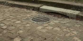 Movie still from “Lupin” (2021), created by Tigran Rosine – View of a manhole cover on the sidewalk; Extreme Close Up shot, High angle