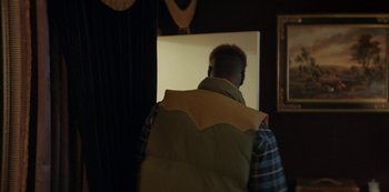 Movie still from “Lupin” (2021), created by Tigran Rosine – A man wearing a vest in a dark room; Medium shot, Over the shoulder angle