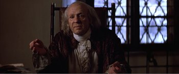 Movie still from “Amadeus” (1984), directed by Milos Forman – An old man sitting in a chair wearing a wig; Medium shot, Low angle
