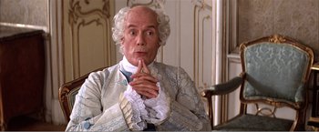 Movie still from “Amadeus” (1984), directed by Milos Forman – An older man in a period costume is sitting at a table; Medium shot, Over the shoulder angle