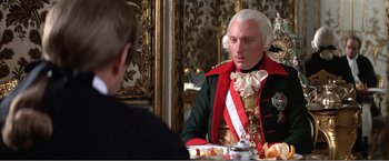 Movie still from “Amadeus” (1984), directed by Milos Forman – A man dressed in period clothing sitting at a table; Close Up shot, Over the shoulder angle