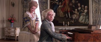 Movie still from “Amadeus” (1984), directed by Milos Forman – A man in a wig playing the piano in front of a woman; Medium shot, Low angle