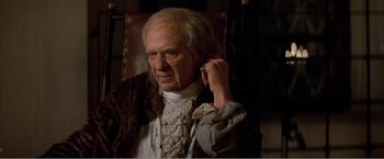 Movie still from “Amadeus” (1984), directed by Milos Forman – An old man talking on a cell phone while sitting in a chair; Close Up shot, High angle