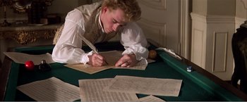 Movie still from “Amadeus” (1984), directed by Milos Forman – A young man writing on a sheet of paper on top of a table; Medium shot, High angle