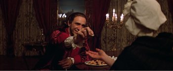 Movie still from “Amadeus” (1984), directed by Milos Forman – A man in a red and black outfit holding a plate of food in front of him; Medium shot, Over the shoulder angle
