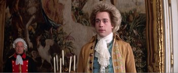 Movie still from “Amadeus” (1984), directed by Milos Forman – A man in a wig and a wig stand in front of candles; Close Up shot, Over the shoulder angle