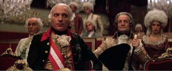 Movie still from “Amadeus” (1984), directed by Milos Forman – A man in a suit sitting in front of another man in a suit; Medium shot, Low angle