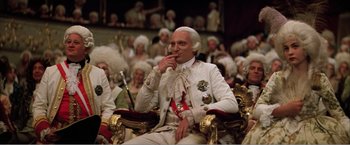 Movie still from “Amadeus” (1984), directed by Milos Forman – A man sitting in a chair in front of a group of people; Medium shot, High angle