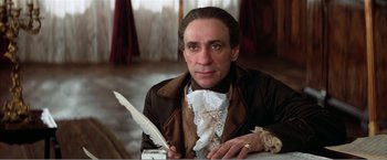 Movie still from “Amadeus” (1984), directed by Milos Forman – A man sitting at a table holding a feather pen; Close Up shot, Low angle