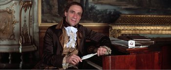 Movie still from “Amadeus” (1984), directed by Milos Forman – A man in a brown and white suit holding a knife; Medium shot, High angle