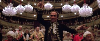 Movie still from “Amadeus” (1984), directed by Milos Forman – A man in a black and white outfit raising his hand in front of an audience; Medium shot, Low angle