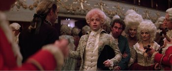 Movie still from “Amadeus” (1984), directed by Milos Forman – A man with a pink wig is standing next to other people; Medium shot, Over the shoulder angle
