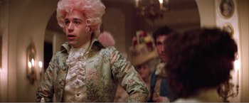 Movie still from “Amadeus” (1984), directed by Milos Forman – A man with a pink wig is standing in front of other people; Medium shot, Over the shoulder angle