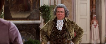 Movie still from “Amadeus” (1984), directed by Milos Forman – An older man in a wig and wig stands in front of a painting; Medium shot, Low angle