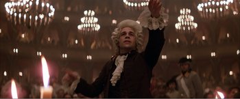 Movie still from “Amadeus” (1984), directed by Milos Forman – A man wearing a wig and a wig stand in front of a chandelier; Medium shot, Low angle