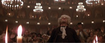 Movie still from “Amadeus” (1984), directed by Milos Forman – A man wearing a wig and wig stands in front of an audience; Medium shot, Low angle