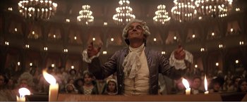 Movie still from “Amadeus” (1984), directed by Milos Forman – A man in a wig and wig stands in front of a group of people; Medium shot, Low angle