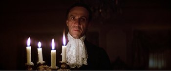Movie still from “Amadeus” (1984), directed by Milos Forman – A man in a white shirt and a white lace collar is holding two lit candles in front of him; Close Up shot, Low angle
